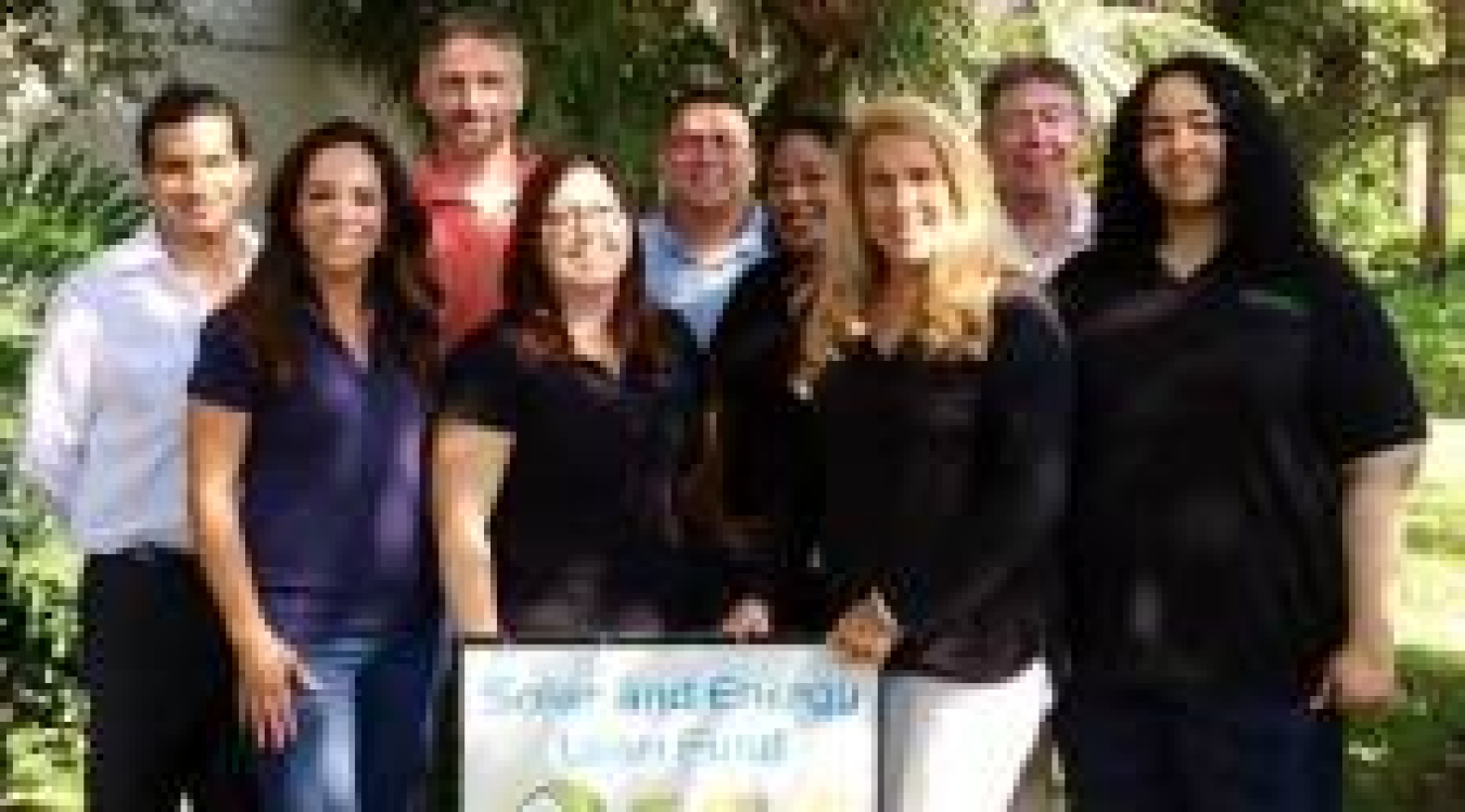 Photo of a group of people standing with a sign looking at the camera.