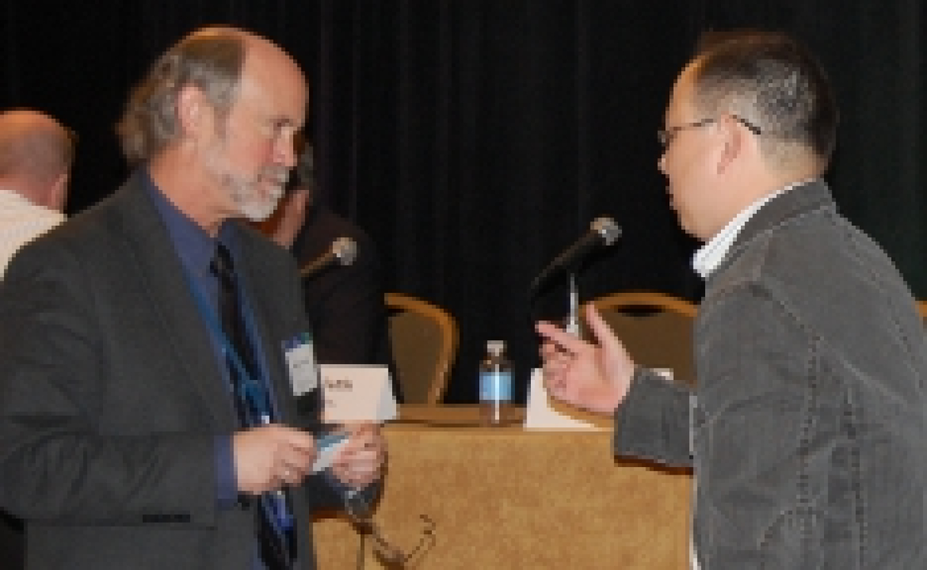 Photo of an attendee asking a question to a panel speaker, who is holding a business card.