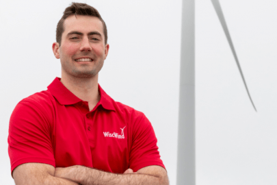 A student in a red shirt stands in front of a wind turbine on a cloudy day. 