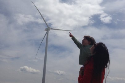 A NREL employee's daughter points at the turbines while in her mother's arms at the National Wind Technology Center.
