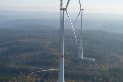 During construction, workers climb out on top of a tall wind turbine and guide 19-ton turbine blades into place.