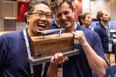 Two young men smile while holding up a 1st place Collegiate Wind Competition trophy.
