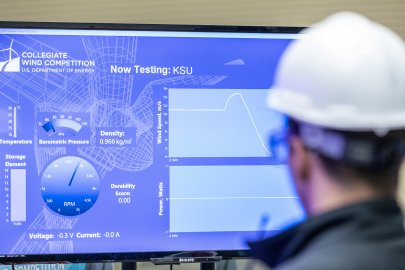 Student in a hard hat stands in front of a monitor.