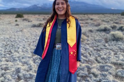 A young woman stands against a sunset smiling. 