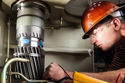 A researcher leans over a wind turbine gearbox to test instrumentation.