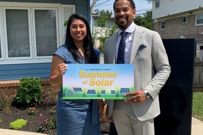 Two people standing in front of a home with solar panels holding a sign that says "Summer of Solar"