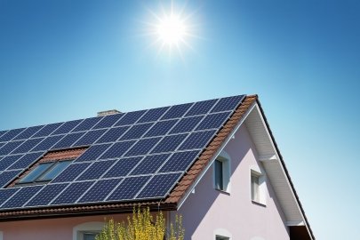 A house with rooftop solar panels and the sun shining above it. 