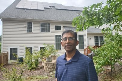 A person standing in front of a house with solar panels on the roof