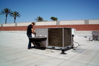 A man on the roof of a commercial building working on a rooftop HVAC unit.