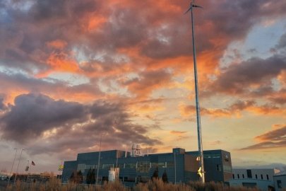 Small wind turbine stands beside a building at sunset.