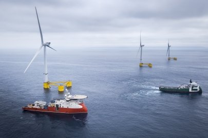 Photo of three offshore wind turbines with two ships in the foreground.