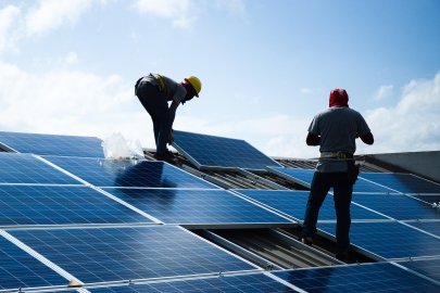 Two people installing large solar panels on a roof.