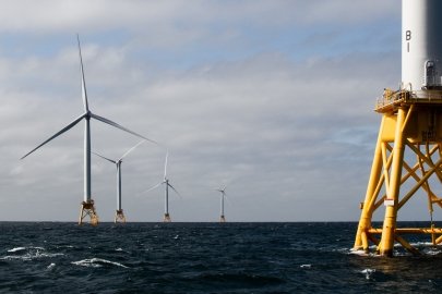 Offshore wind turbines at sea with sun shining.