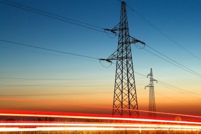 Transmission lines along the side of the road at dusk. Cars zip by leaving only the after shine of their headlights. 