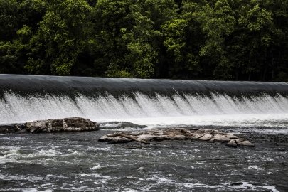 A small dam spanning a river with dense trees along the shore.