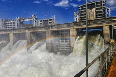 A rainbow forms across a waterfall created by a dam.