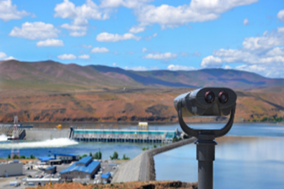 A dam on a river as seen from behind a viewing machine positioned on a hill nearby.