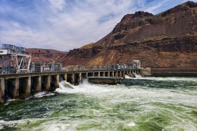 A dam creates churning waters in a river flowing between red hills.