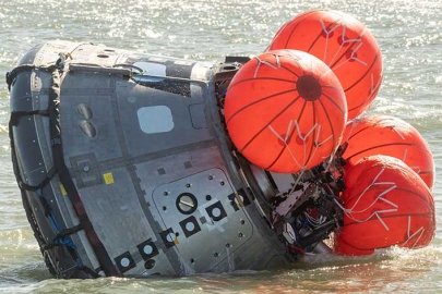 A small metallic pod floats on the ocean surface, slightly tilted on its side, as four orange balloons inflate on one end.