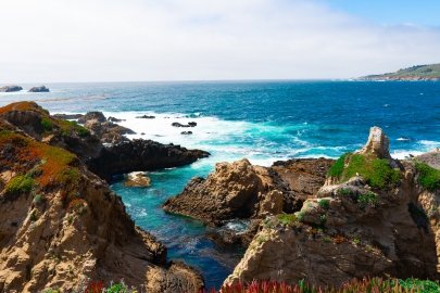 Ocean waves flow into a channel between tall, craggy rocks along a coastline.