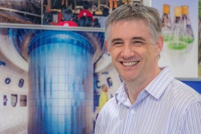 Richard Buttery, Director of the DIII-D National Fusion Facility, stands in front of an image showing the interior of the DIII-D tokamak.