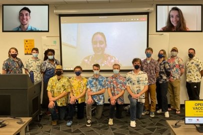 Members of the WindJax Energy Club standing at the front of a classroom wearing medical masks and Hawaiian shirts. A few students are projected on screens behind them. 