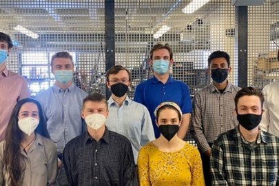 A group of young men and women wearing face masks in a laboratory or workshop setting.