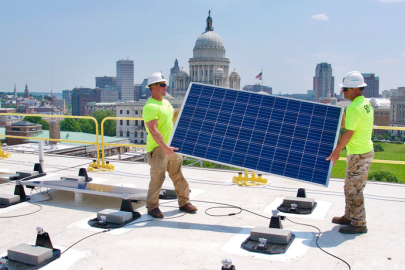 Two men installing solar panels on the roof of a government building in Rhode Island.
