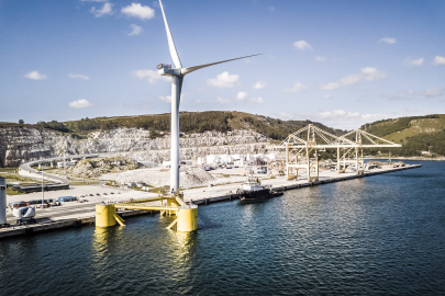 A wind turbine floating just off a dock.