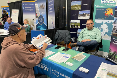 Givey Kochanowski sits in the Arctic Energy Office booth and talks to an Alaskan Native stakeholder. 