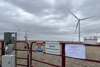 Several wind turbines are scattered behind a fence. 