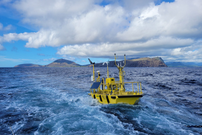 A buoy with lots of instruments floats in the ocean with an island in the background.