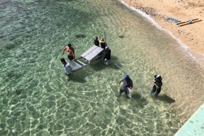 A group of people wade into the water off a beach, carrying a metal device into the water. 