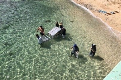 A group of people wade into the water off a beach, carrying a metal device into the water.