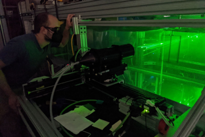 Person with eye protection looking at green beams of light in a contained clear box. 