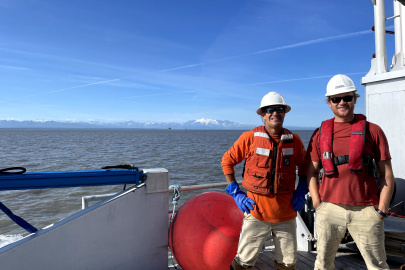 Two men in hard hats standing on the deck of a boat. 