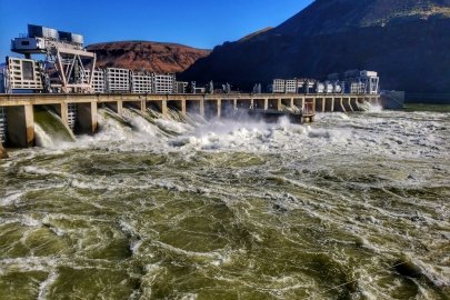 Water rushes through a hydropower facility with reddish hills in the background