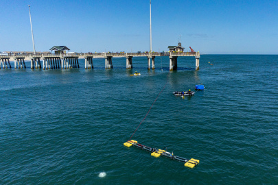A photo of wave-powered desalination devices, boats, and people in the ocean near a pier.