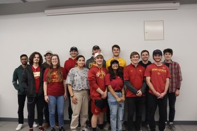 Two rows of students wearing Iowa State University apparel standing in a room against a wall.