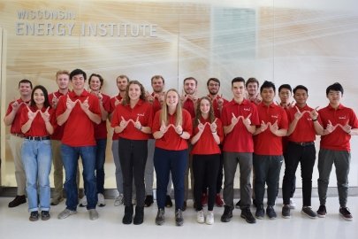 Two rows of students in matching red shirts holding their thumbs and pointer fingers in the shape of a W.
