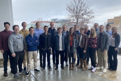 Two rows of students standing on sidewalk surrounded by buildings.