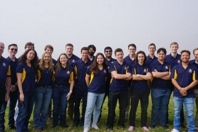 Two rows of students in matching shirts standing in a grassy area.