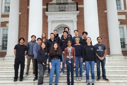 Three rows of students standing on steps in front of a large brick building labeled “Gilman Hall.”