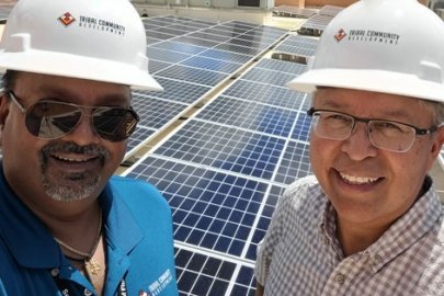Two men with hard hats pose with roof top solar panels.