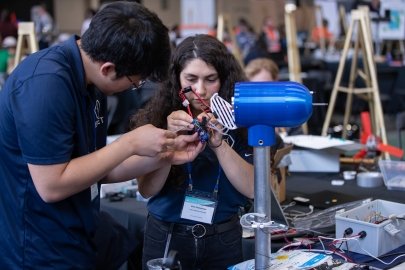 Two students with name tags adjusting the wiring of a model wind turbine.