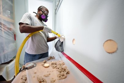 Man wearing a protective mask and working on an interior wall in a building as part of a retrofit project.