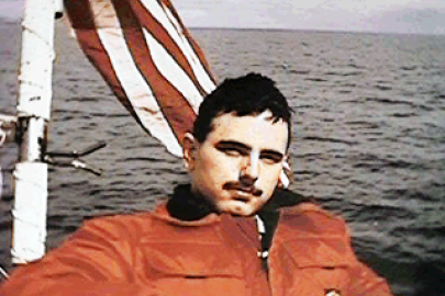 Man in a jacket on a boat that is flying the American flag behind him