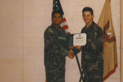 Two men in military uniforms shake hands and one is presented with a certificate