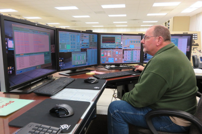 An employee sits looking at computer monitors. 