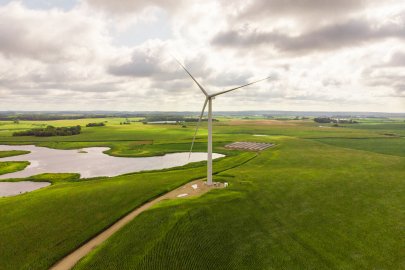 A large wind turbine on a grassy plain near a solar photovoltaic array and a lake.
